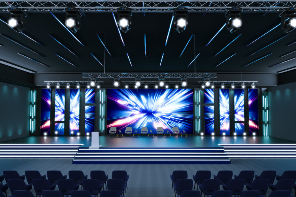 Conference stage with LED video walls, truss lighting, and rows of audience chairs set for a product launch