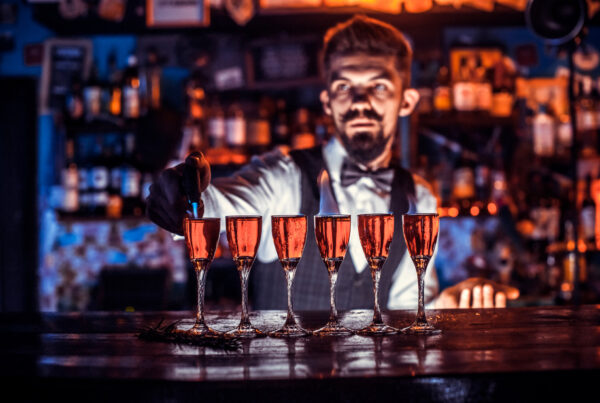 Bartender preparing a row of pink cocktails on the bar counter