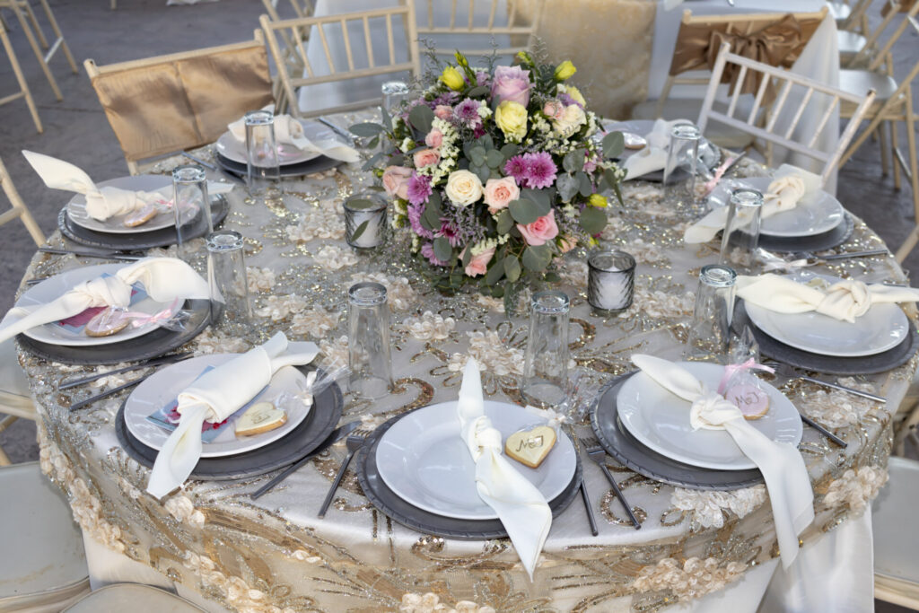 Elegant round wedding reception table with floral centerpiece, white plates, folded napkins and lace tablecloth