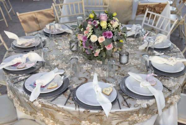 Elegant round wedding reception table with floral centerpiece, white plates, folded napkins and lace tablecloth