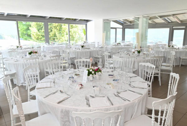 Banquet hall with multiple round tables set with white linens, place settings and white chairs for a wedding reception