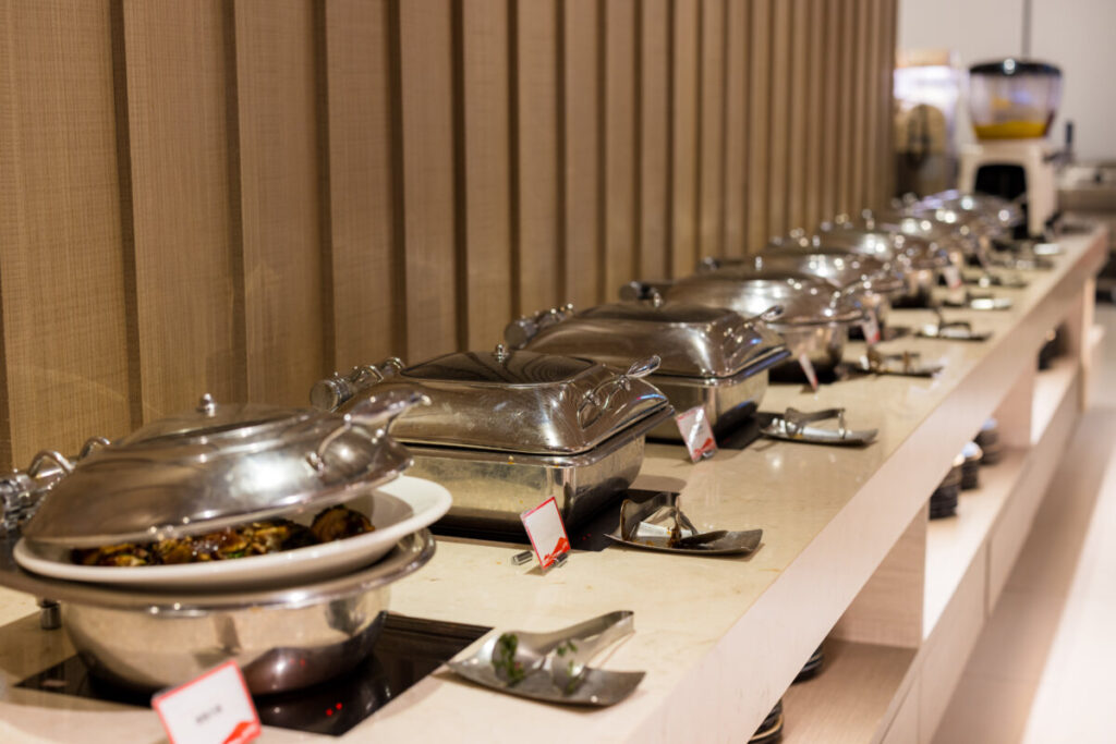 Line of stainless steel chafing dishes on a buffet counter with serving utensils