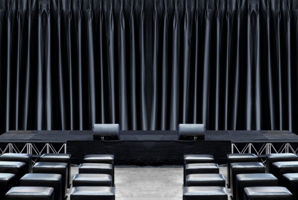 Event stage with black skirting around the platform, black drapery backdrop, and rows of seating