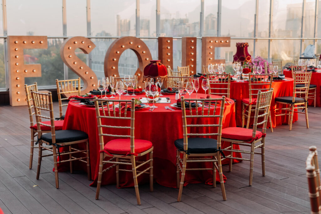 Rooftop wedding reception with red-draped round tables, gold chiavari chairs, and marquee letters against city views