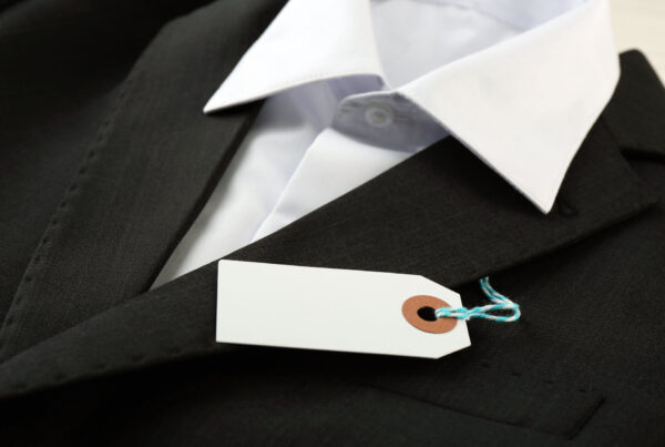 Dark suit jacket with a blank white tag tied on with blue string, like a coat check ticket