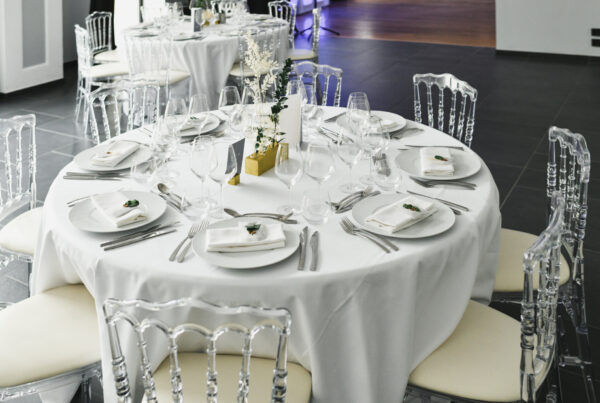 Clear acrylic ghost chairs with white cushions around a round banquet table set with white linens and place settings